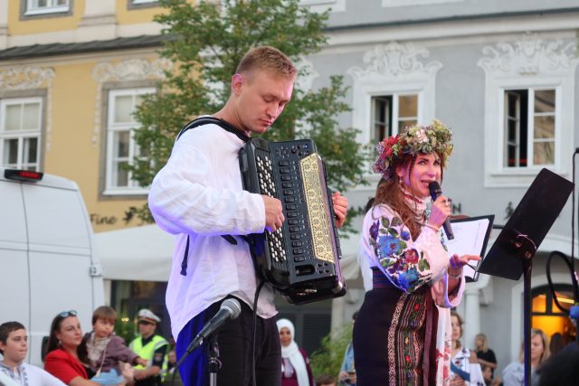 Eine ukrainische Band steht auf der Bühne. Eine Sängerin mit Blumenkranz ist zu sehen. Ein Mann spielt Akkordeon.