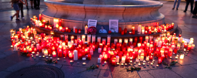 Vor einem Springbrunnen stehen ganz viele angezündete Kerzen, Blumen und ein Bild von Lisa-Maria Kellermayr