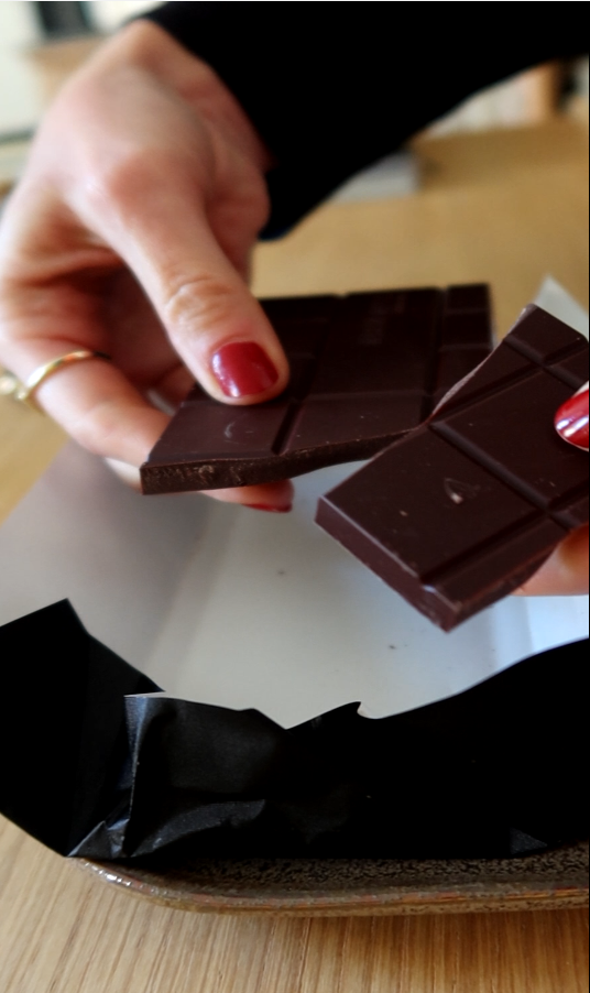 Eine manikürte Hand bricht gerade eine Schokoladentafel.