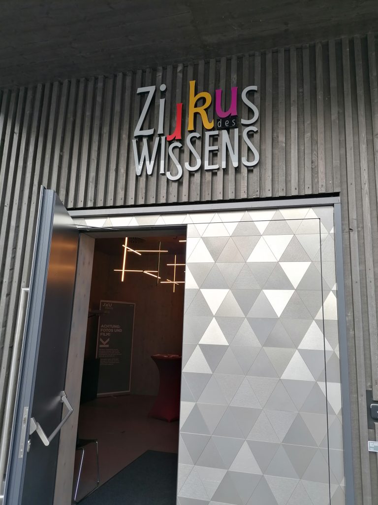 Eingang eines Gebäudes. Über der silberenen Doppeltür steht der Schriftzug "Zirkus des Wissens"