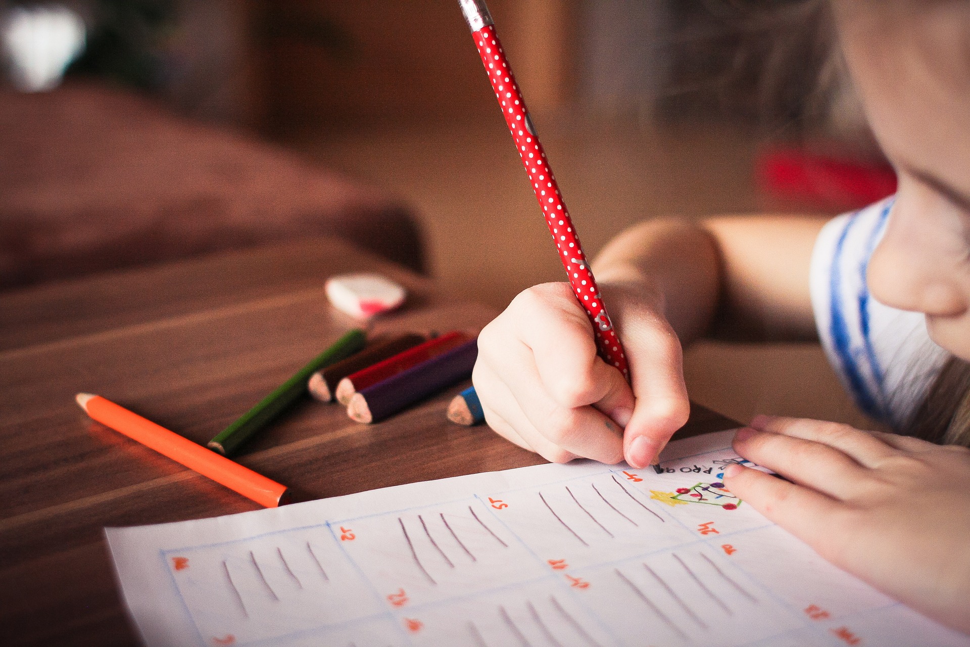 Ein Kind ist über einen Zettle gebeugt und füllt diesen mit einem Stift aus.