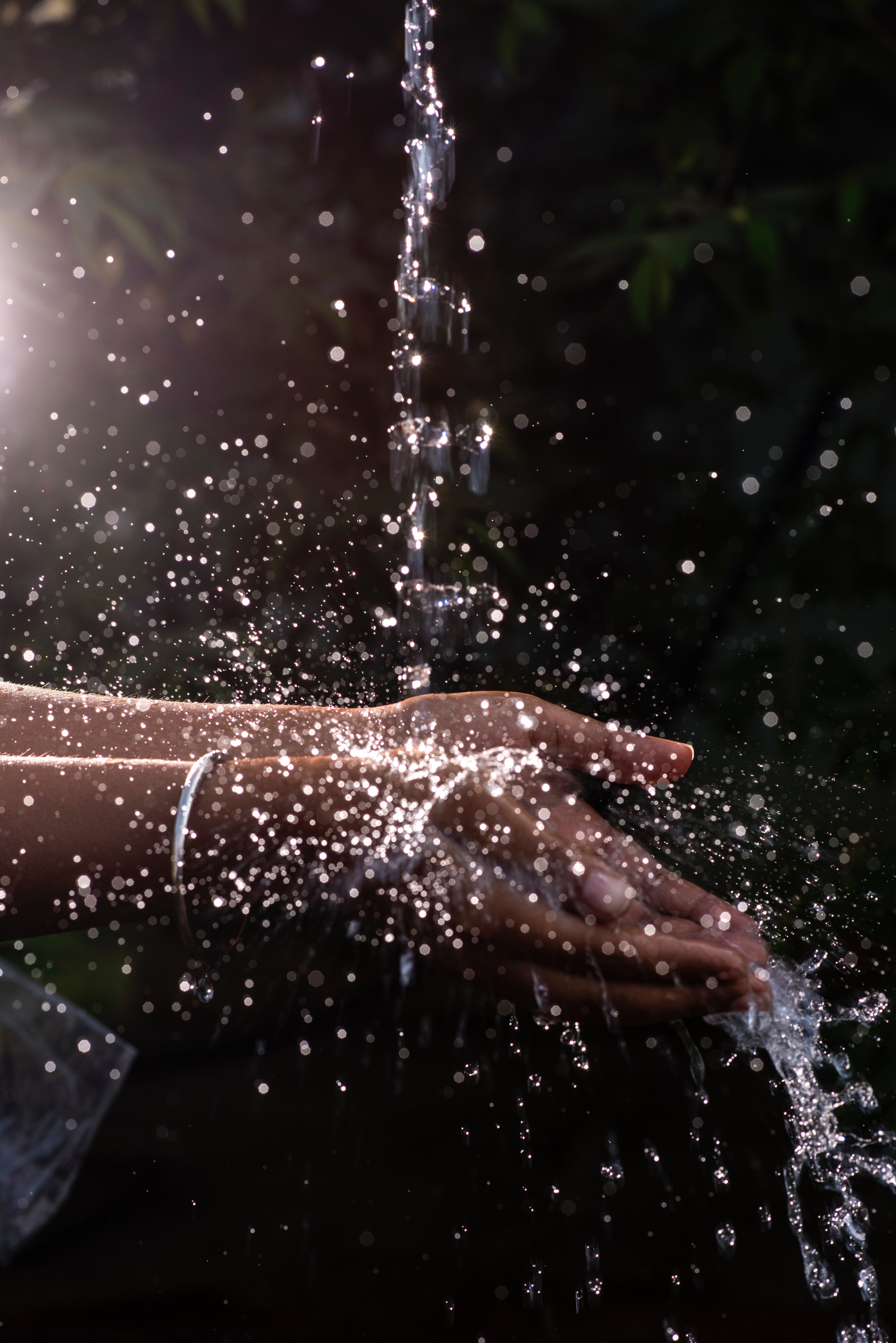 Über Hände fließt Wasser von oben. Es spritzt über die Fingerspitzen