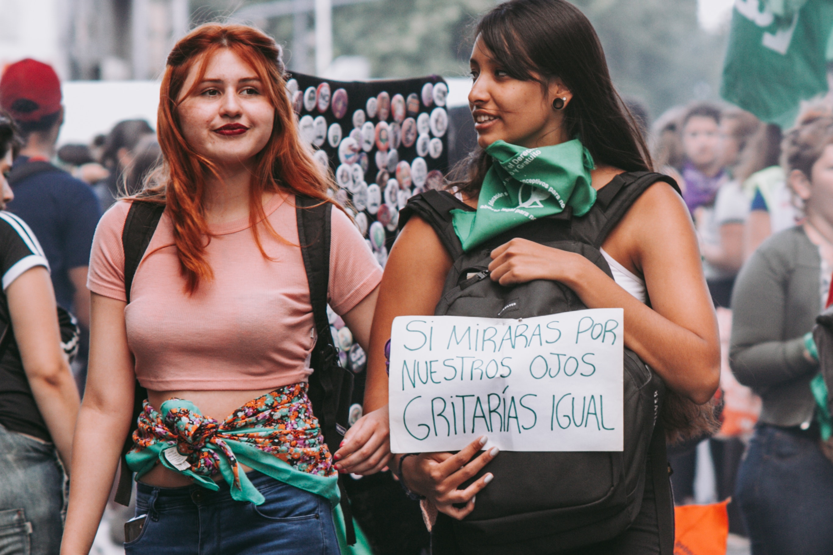 Zwei Frauen sind von vorne zu sehen. Sie befinden sich auf einer Demonstration und halten ein spanisches Demoschild vor der Brust.