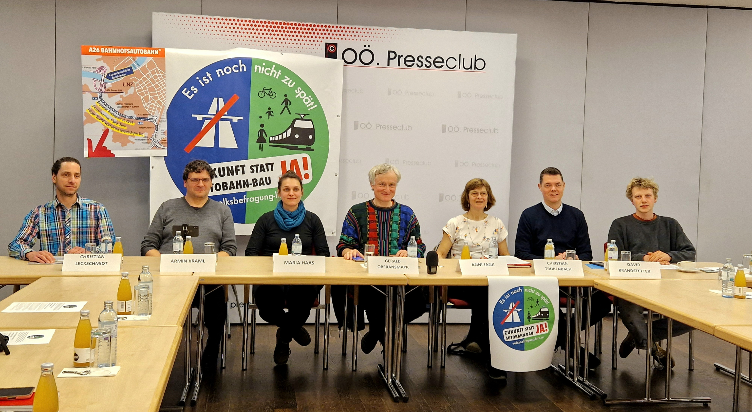 Menschen sitzen an einem langen Tisch. Sie sind bei einer Pressekonferenz. Vor ihnen stehen Namenskarten und Wasserflaschen