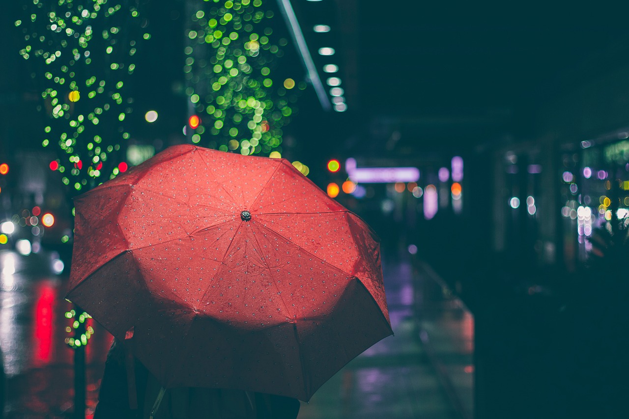 Man sieht eine Person von hinten. Ihr Körper wird von einem großen roten Regenschirm fast vollständig verdeckt. 