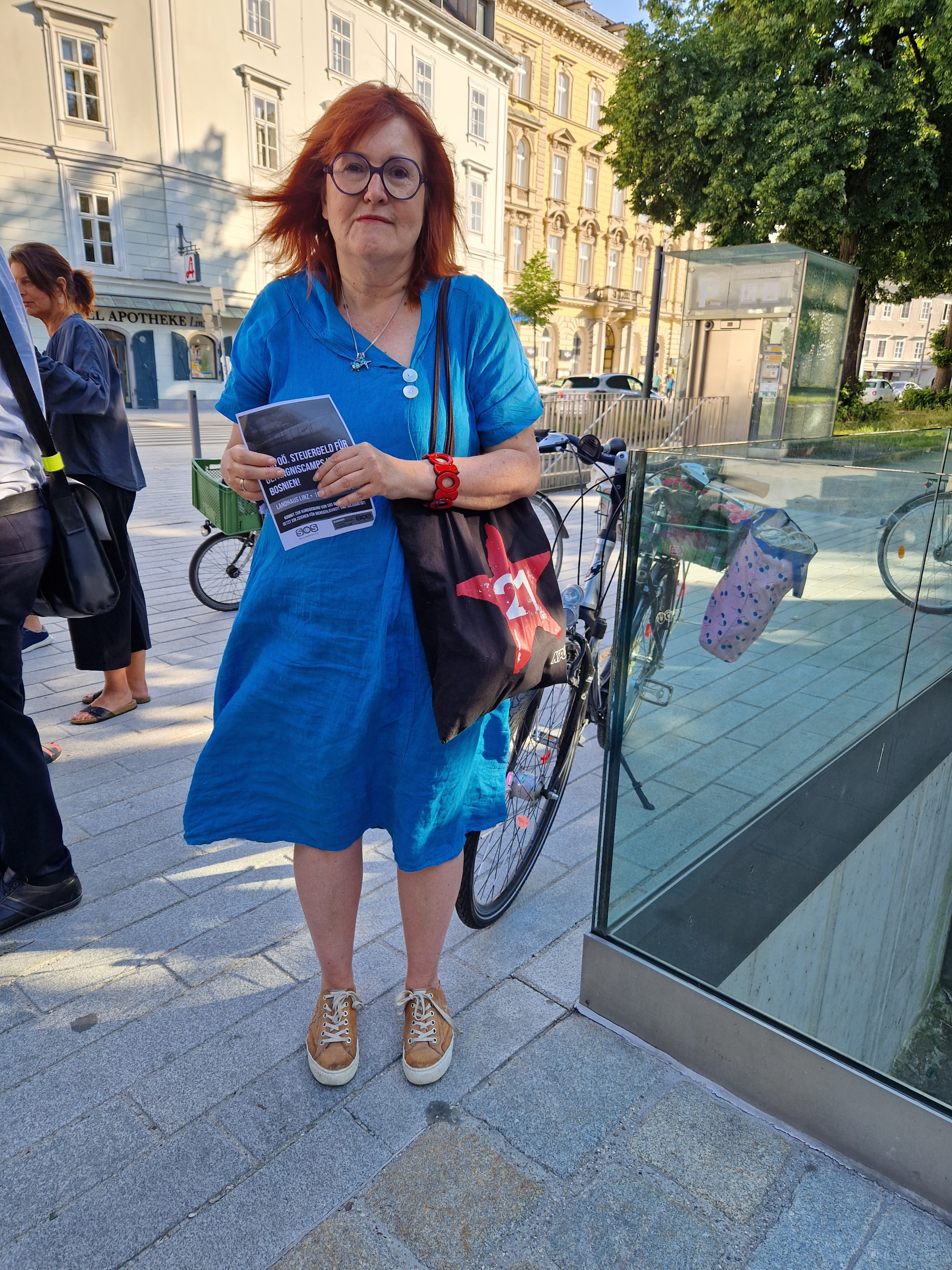 Eine Frau in einem blauen Kleid hält einen Flyer von SOS Balkanroute hoch
