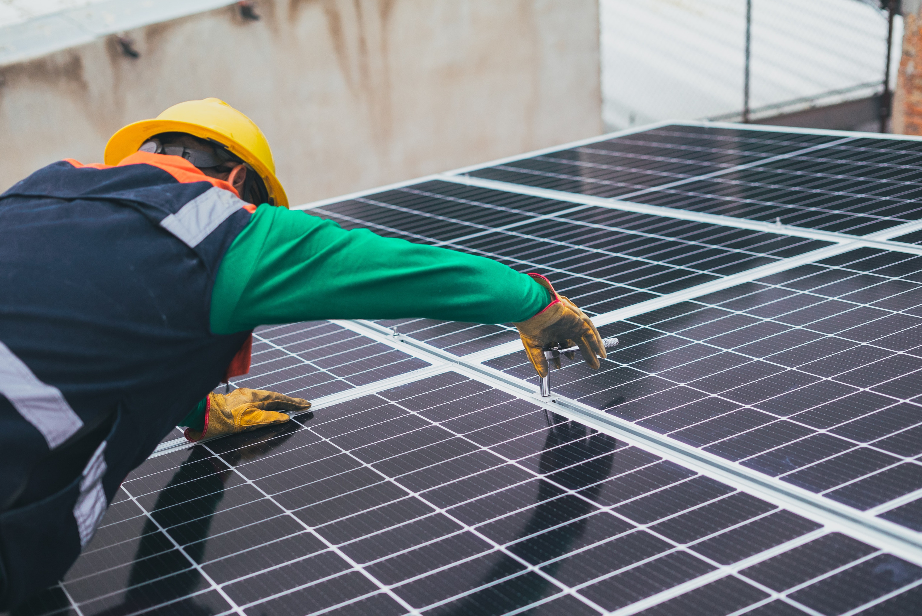 Eine Person mit gelben Bauhelm verschraubt ein Solarpanel