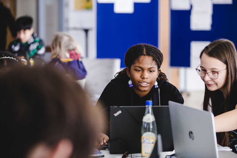 Jugendliche sitzen vor Laptops und bearbeiten gemeinsam an einem Coding Projekt