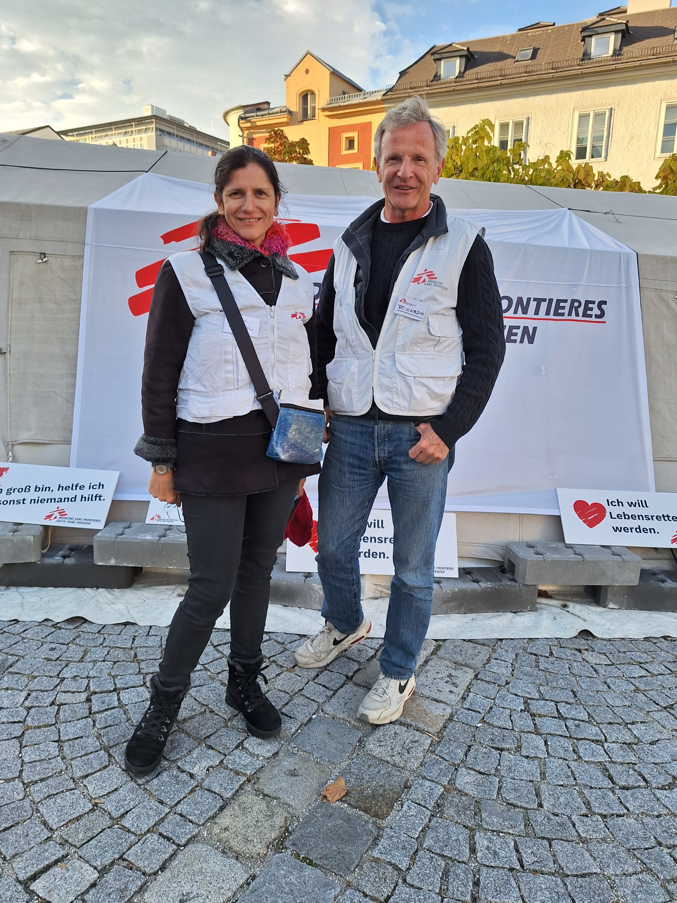 2 Menschen stehen vor einem Zelt von Ärzte ohne Grenzen. sie haben weiße Westen über der Kleidung an.