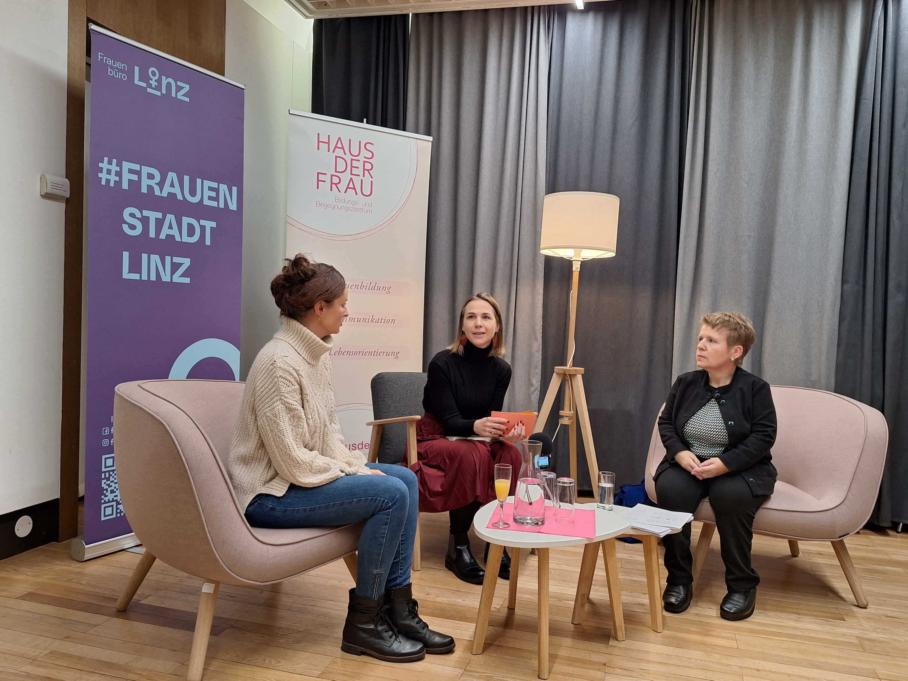 3 Frauen sitzen auf gemütlichen Sesseln und sprechen miteinander. Vor ihnen steht ein niedriges Tischchen. Sie sitzen in einem kleinen Vortragsraum.