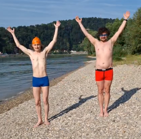 2 männlich gelesene Personen machen Aufwärmübungen in Schwimmanzügen