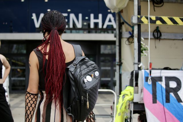 Eine Frau ist von hinten vor dem Wiener Hauptbahnhof zu sehen. Sie trägt rote Braids und einen schwarzen Rucksack.