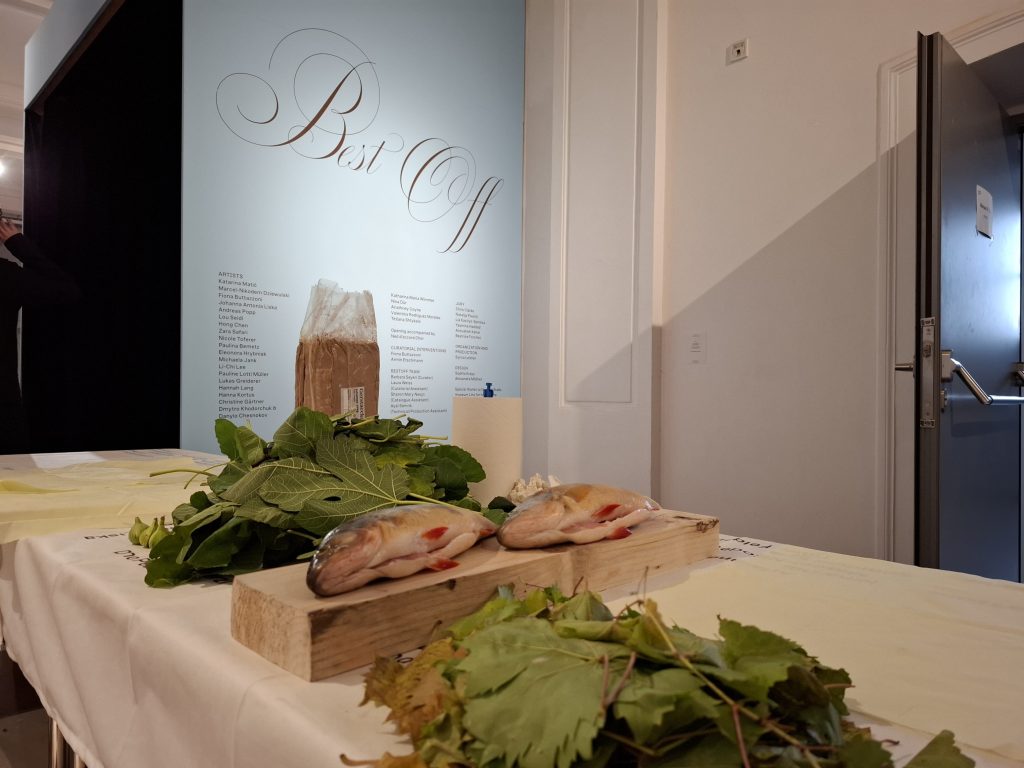 zwei Fische liegen vor dem Best Off Ausstellungstext auf einem Tisch mit Blättern und einer Packung Ton